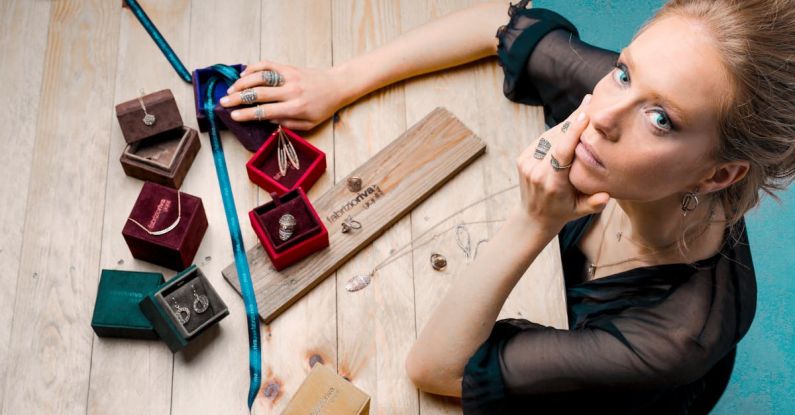 Small Business Success - From above serious businesswoman looking up at camera while sitting at wooden table with small jewelry boxes with bijouterie and decorating with ribbon as present